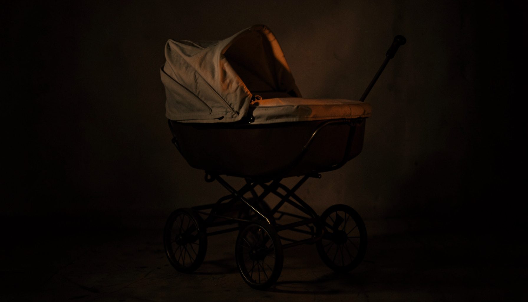 Vintage baby carriage standing in soft, low light with deep brown shadow tones and warm cream highlights